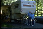 Volunteer campground hosts standing in front of their trailer.