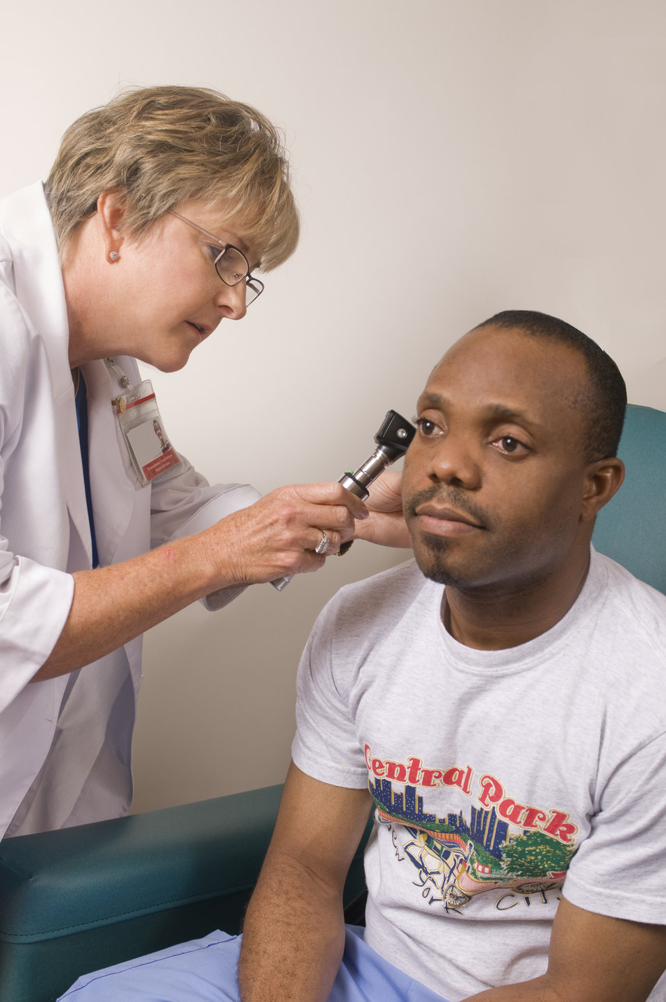 This image depicts a female clinician conducting an examination of a male patient's right ear, using an otoscope, which she'd inserted into 