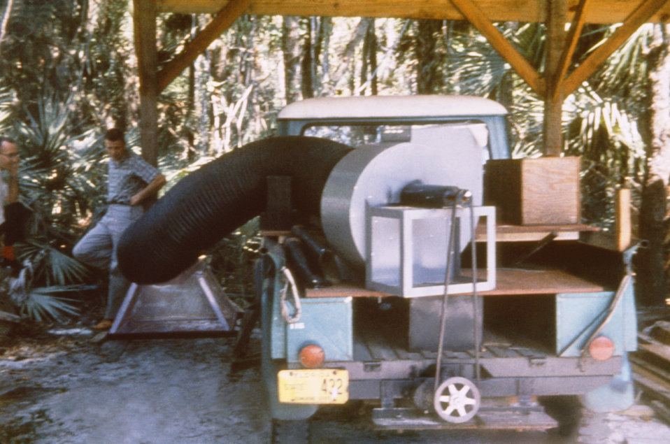 This is a 1965 photograph of a giant mosquito vacuum mounted on truck used in collecting mosquitoes alongside residential areas.