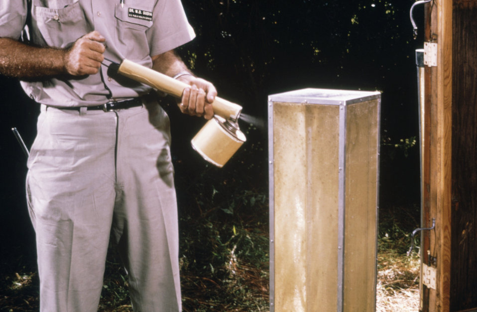 This field researcher is using a hand-held sprayer to knock down mosquitoes on the screen of a horse stable mosquito trap.